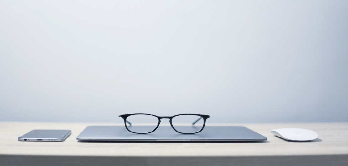 Image of eye glasses sitting on a closed laptop next to a cell phone and mouse.